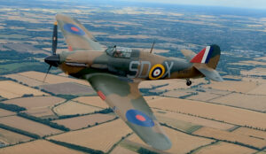 Camouflaged aircraft marked SD-X flying above fields.